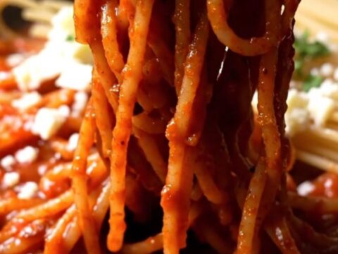 A close-up of crispy, charred spaghetti in a black cast-iron skillet with a red tomato glaze and fresh stracciatella.