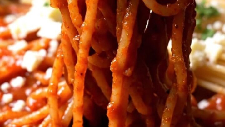A close-up of crispy, charred spaghetti in a black cast-iron skillet with a red tomato glaze and fresh stracciatella.
