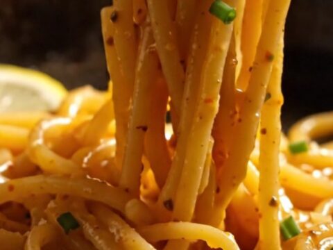 A close-up of bucatini pasta tossed with lump crab and bright red Calabrian chilies in a carbon-steel pan.