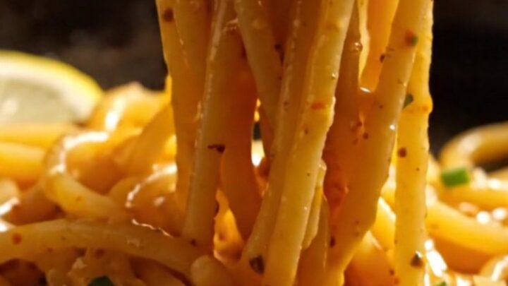 A close-up of bucatini pasta tossed with lump crab and bright red Calabrian chilies in a carbon-steel pan.