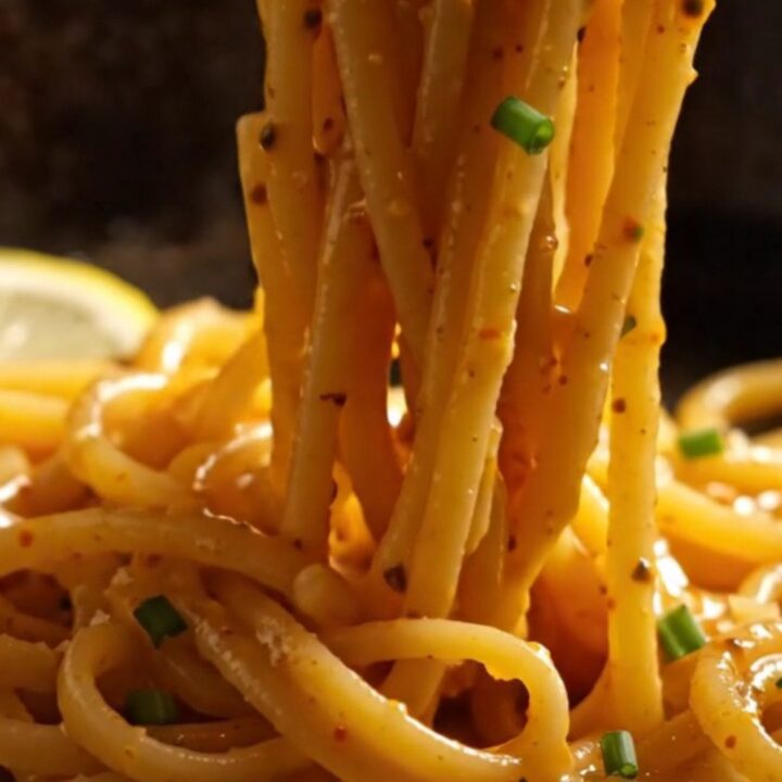 A close-up of bucatini pasta tossed with lump crab and bright red Calabrian chilies in a carbon-steel pan.