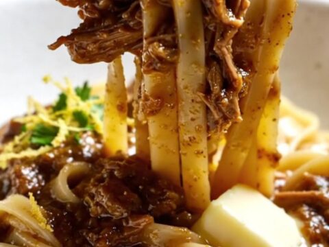 A close-up of fork-shredded braised beef short rib ragu over fresh tagliatelle topped with Parmesan.