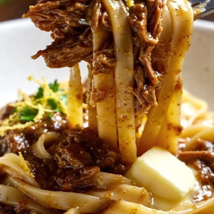 A close-up of fork-shredded braised beef short rib ragu over fresh tagliatelle topped with Parmesan.