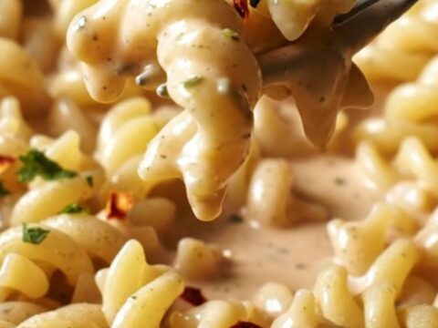 A close-up of creamy garlic and herb Boursin pasta with roasted red peppers in a ceramic dish.