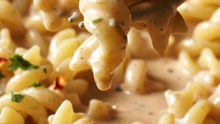 A close-up of creamy garlic and herb Boursin pasta with roasted red peppers in a ceramic dish.