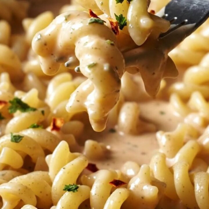 A close-up of creamy garlic and herb Boursin pasta with roasted red peppers in a ceramic dish.