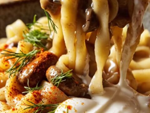 A close-up of creamy mushroom Stroganoff with wavy noodles, garnished with fresh dill and smoked paprika.