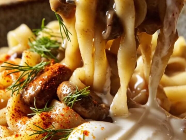 A close-up of creamy mushroom Stroganoff with wavy noodles, garnished with fresh dill and smoked paprika.