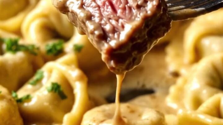 A close-up of seared ribeye steak bites resting on a bed of cheese tortellini in a creamy Parmesan sauce.