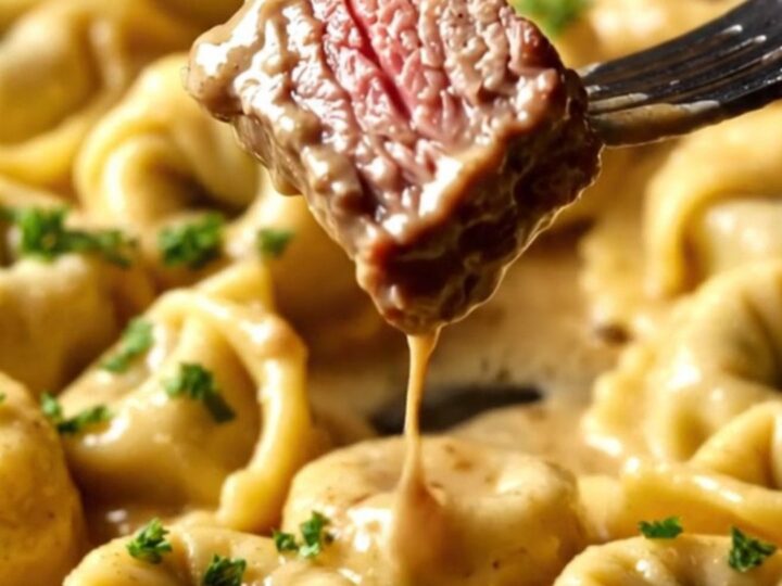 A close-up of seared ribeye steak bites resting on a bed of cheese tortellini in a creamy Parmesan sauce.