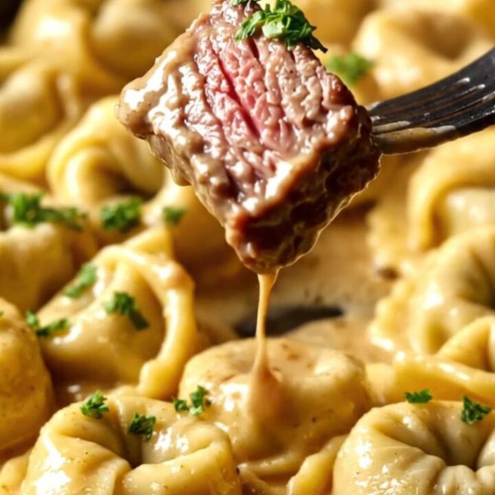 A close-up of seared ribeye steak bites resting on a bed of cheese tortellini in a creamy Parmesan sauce.