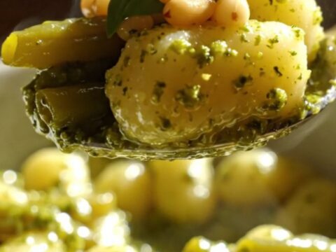 A close-up of vibrant green pesto gnocchi with green beans and golden toasted pine nuts in a bowl.