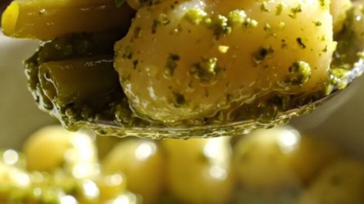 A close-up of vibrant green pesto gnocchi with green beans and golden toasted pine nuts in a bowl.