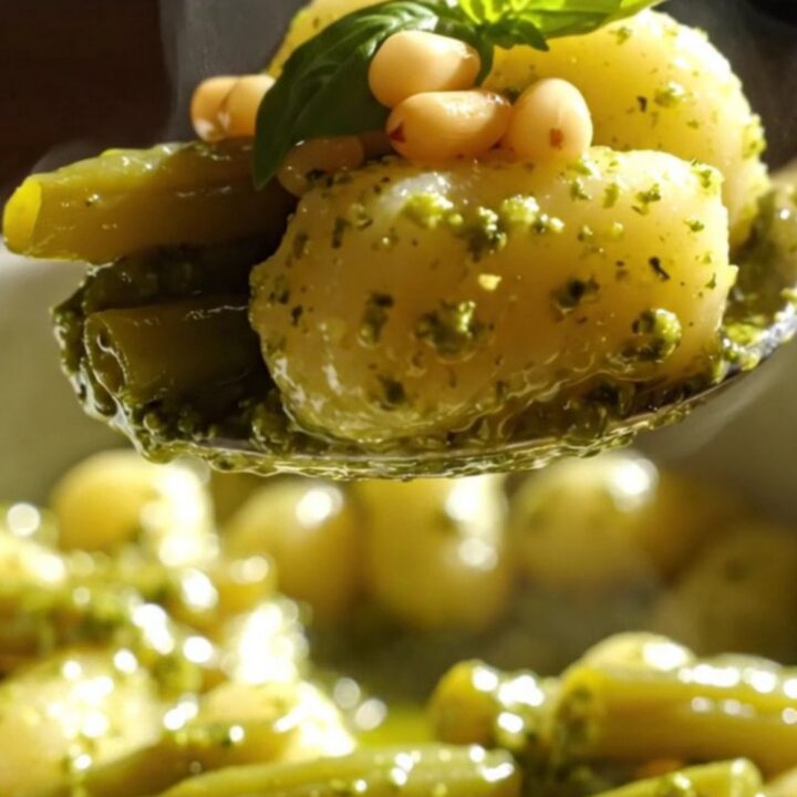 A close-up of vibrant green pesto gnocchi with green beans and golden toasted pine nuts in a bowl.
