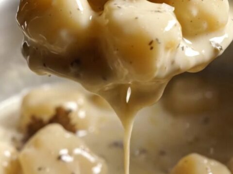 A close-up of pillowy gnocchi coated in a glossy, rich white sauce with visible black truffle shavings.