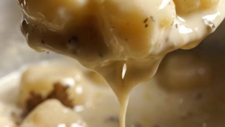 A close-up of pillowy gnocchi coated in a glossy, rich white sauce with visible black truffle shavings.