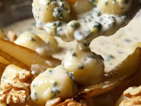 A copper skillet filled with creamy Gorgonzola gnocchi topped with golden caramelized pear slices and walnuts.