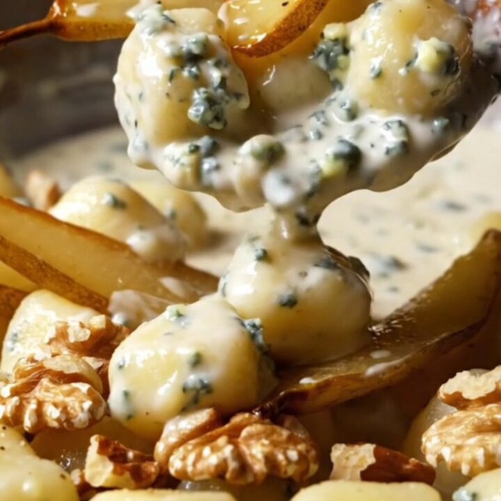 A copper skillet filled with creamy Gorgonzola gnocchi topped with golden caramelized pear slices and walnuts.