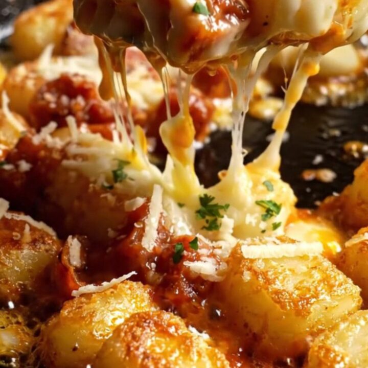 A close-up of crispy pan-fried gnocchi glazed in smoky red chorizo oil and topped with melted, bubbling Manchego cheese.