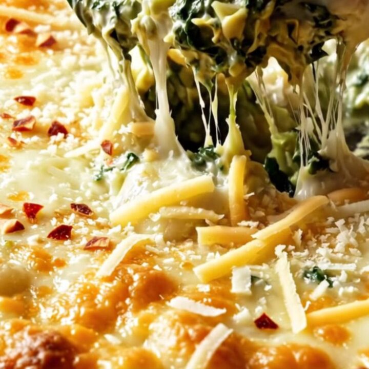 A cast iron skillet filled with a creamy, bubbling spinach and artichoke gnocchi bake with golden melted cheese.