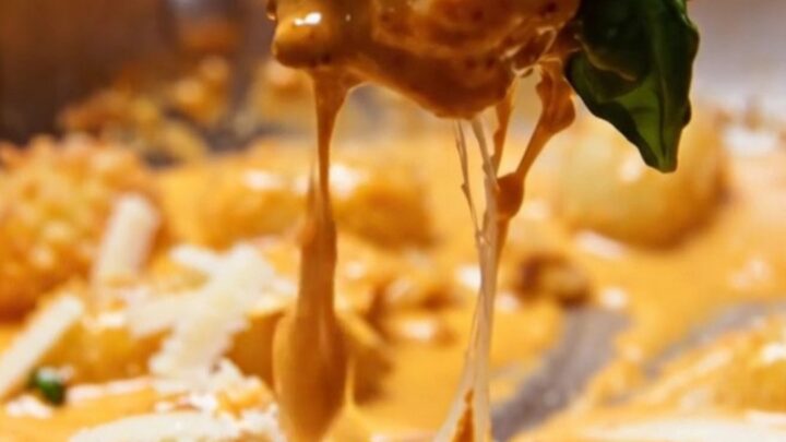 Extreme close-up of golden pan-seared gnocchi coated in a vibrant, velvety orange spicy vodka cream sauce with basil.