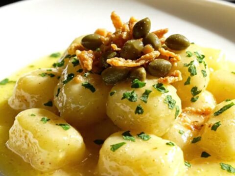 A close-up of golden-seared gnocchi coated in a glossy lemon butter sauce with crispy capers.