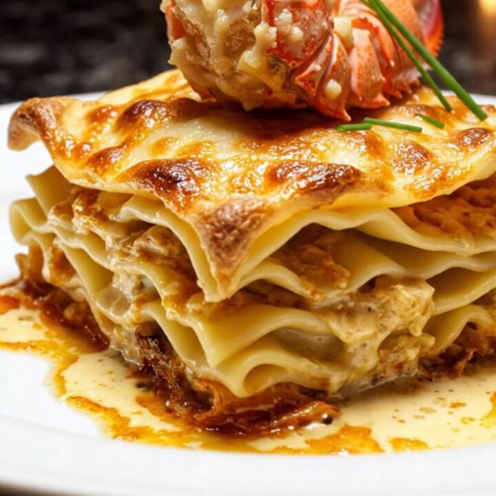 A slice of luxury lobster and Gruyère lasagna with a golden, bubbling cheese crust on a white porcelain plate.