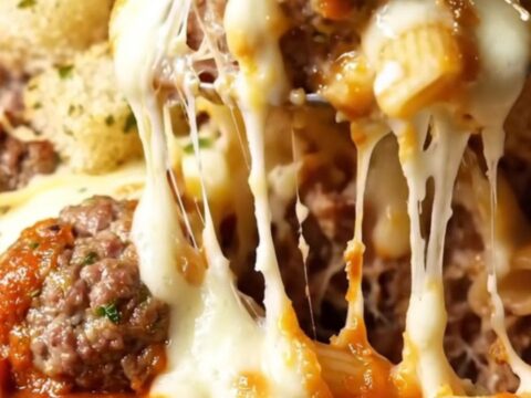 A close-up of a meatball sub pasta bake with melted cheese and crispy garlic bread.