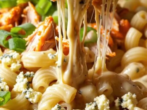 A close-up of a steaming bowl of buffalo pulled chicken mac and cheese topped with gorgonzola and fresh herbs.