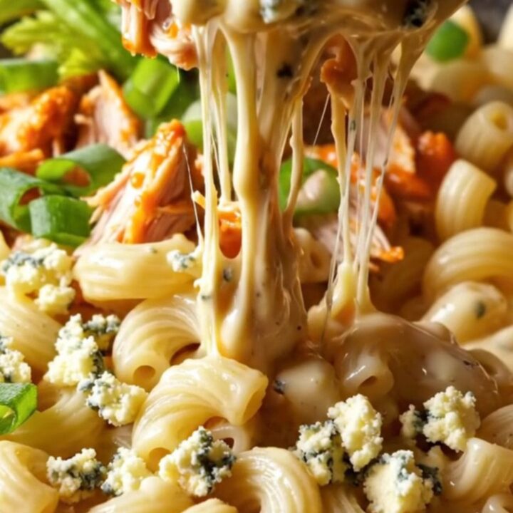 A close-up of a steaming bowl of buffalo pulled chicken mac and cheese topped with gorgonzola and fresh herbs.