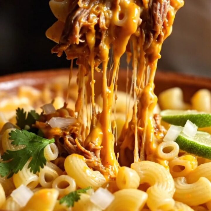 A close-up shot of creamy mac and cheese swirled with spicy red consommé and topped with shredded beef.