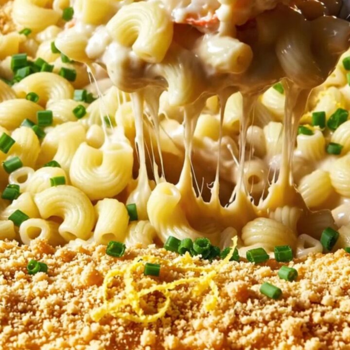 A close-up of a bowl of lobster mac and cheese with visible lobster chunks and a golden breadcrumb topping.