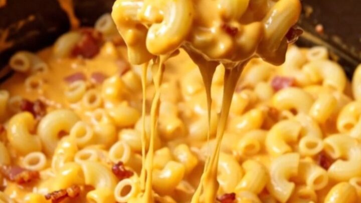 A close-up of a creamy jalapeño popper mac and cheese in a black Dutch oven, topped with crispy bacon and green jalapeños.