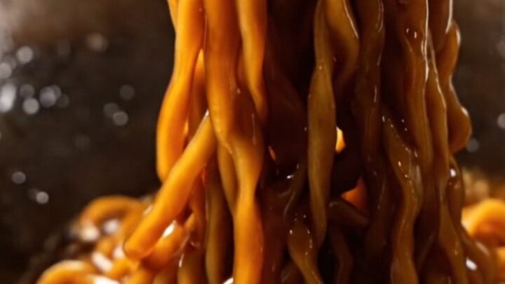 A close-up of glossy dark wheat noodles topped with crispy golden fried scallions.