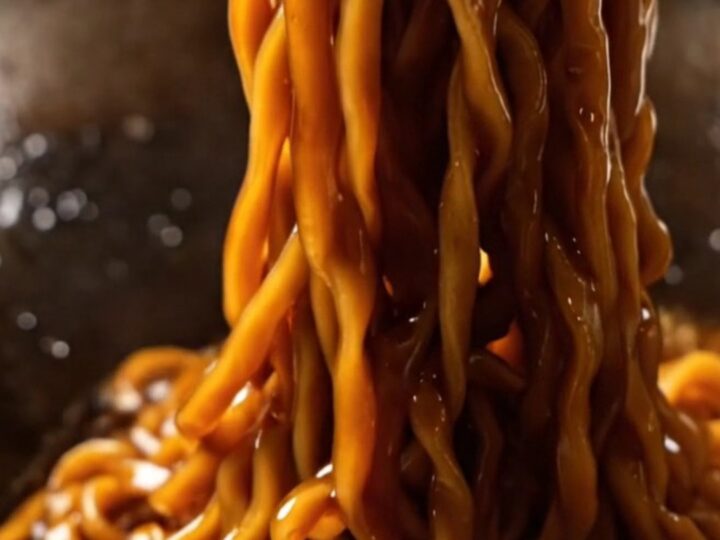 A close-up of glossy dark wheat noodles topped with crispy golden fried scallions.