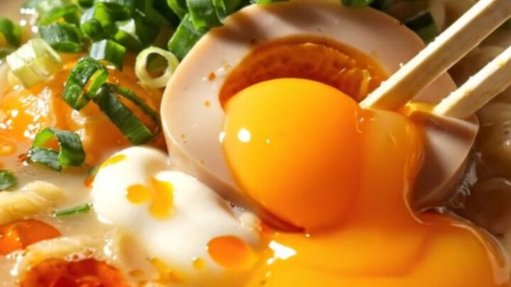 A steaming, creamy bowl of ramen topped with a perfectly jammy orange-yolk egg, fresh scallions