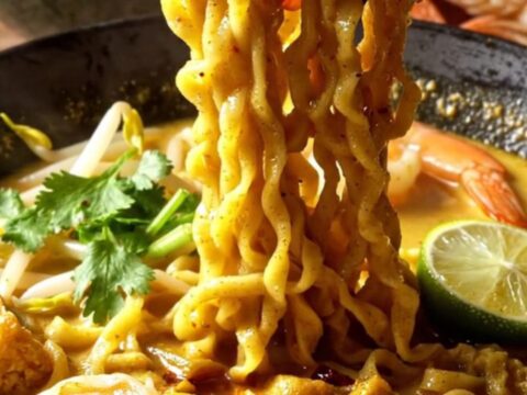 A steaming bowl of creamy coconut curry laksa ramen topped with plump shrimp, tofu puffs, and fresh cilantro.