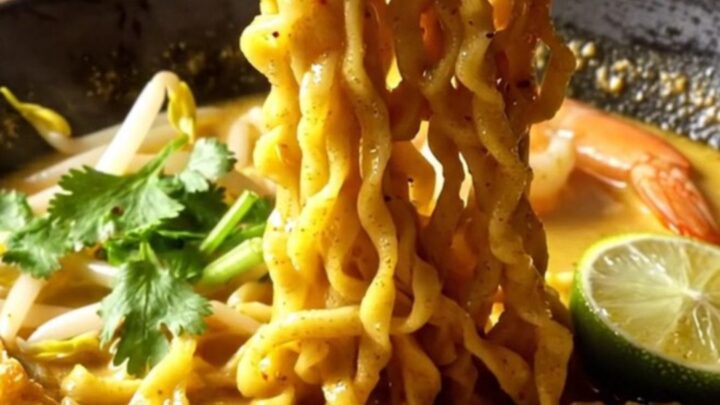 A steaming bowl of creamy coconut curry laksa ramen topped with plump shrimp, tofu puffs, and fresh cilantro.