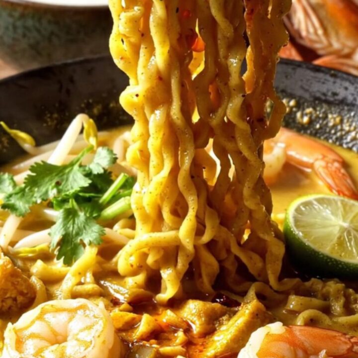 A steaming bowl of creamy coconut curry laksa ramen topped with plump shrimp, tofu puffs, and fresh cilantro.