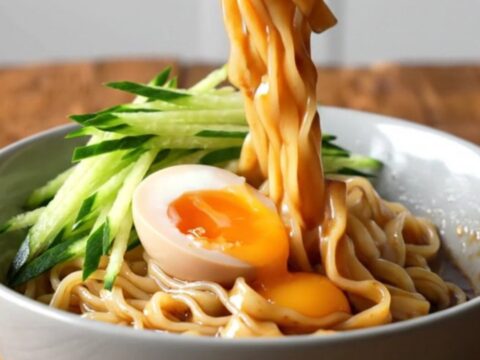 A bowl of wide, glossy noodles coated in a rich, spicy sesame sauce