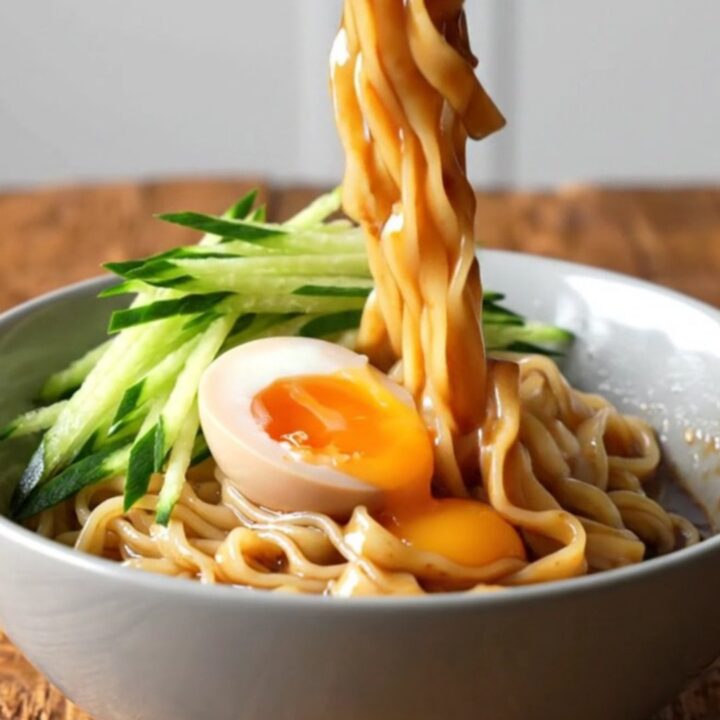 A bowl of wide, glossy noodles coated in a rich, spicy sesame sauce