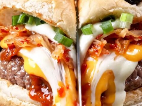 A close-up of a juicy smash burger with a glossy gochujang glaze, melted cheese, and kimchi on a toasted milk bread bun.