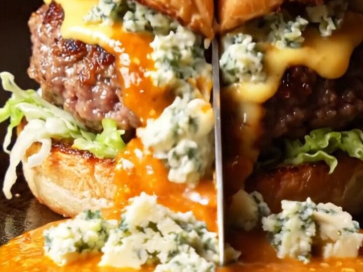 A close-up shot of a blue cheese buffalo smash burger on a brioche bun with fiery sauce dripping down.