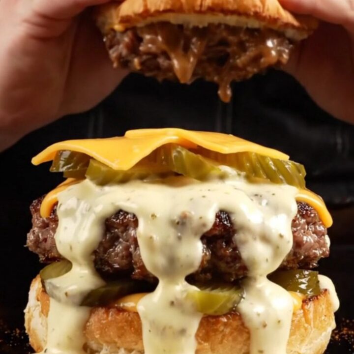 A close-up of a juicy brisket smash burger topped with creamy white sauce and pickles on a toasted bun.