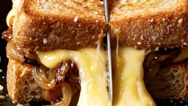 A close-up of a French onion soup grilled cheese with melted Gruyere stretching between two slices of sourdough.