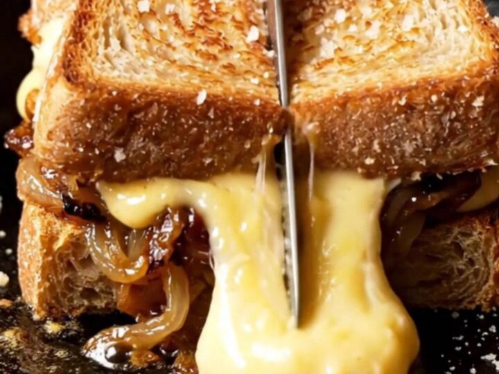 A close-up of a French onion soup grilled cheese with melted Gruyere stretching between two slices of sourdough.