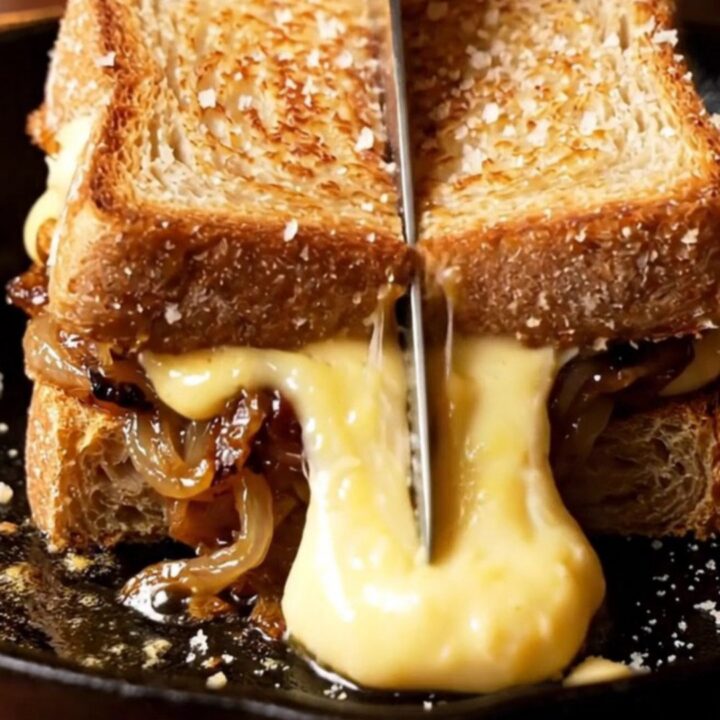 A close-up of a French onion soup grilled cheese with melted Gruyere stretching between two slices of sourdough.