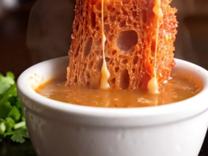 A crispy sourdough birria grilled cheese sandwich with melting Oaxaca cheese, served with a side of hot, red consommé.