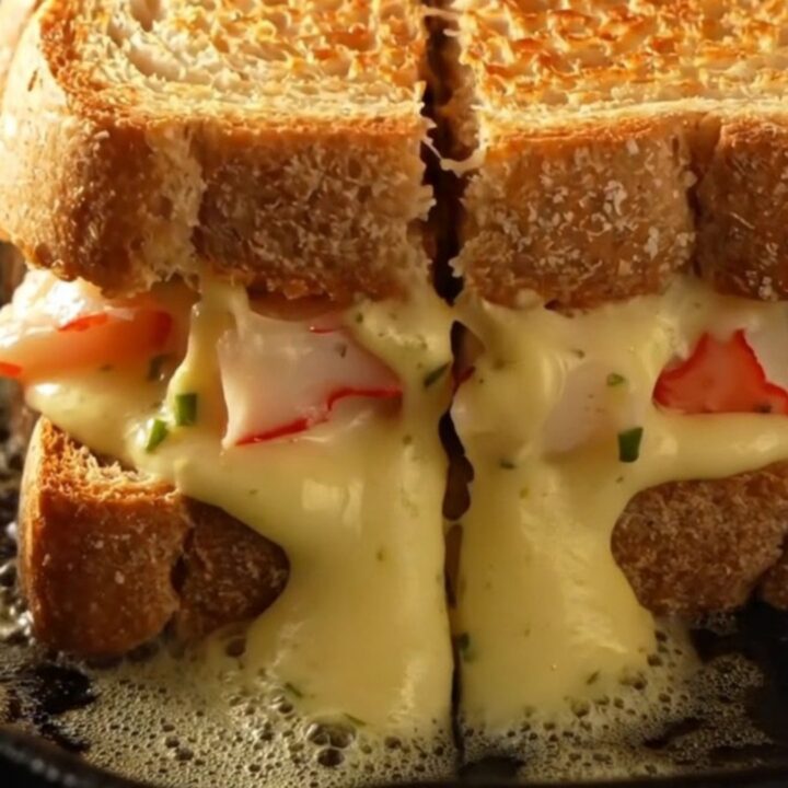 A golden-brown sourdough melt cut in half, showing oozing Gruyère and Fontina cheese with chunks of Maine lobster and lump