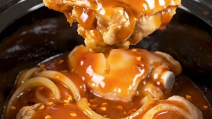 A close-up of tender, braised chicken thighs coated in a rich, dark red honey chipotle sauce with visible onion slices.